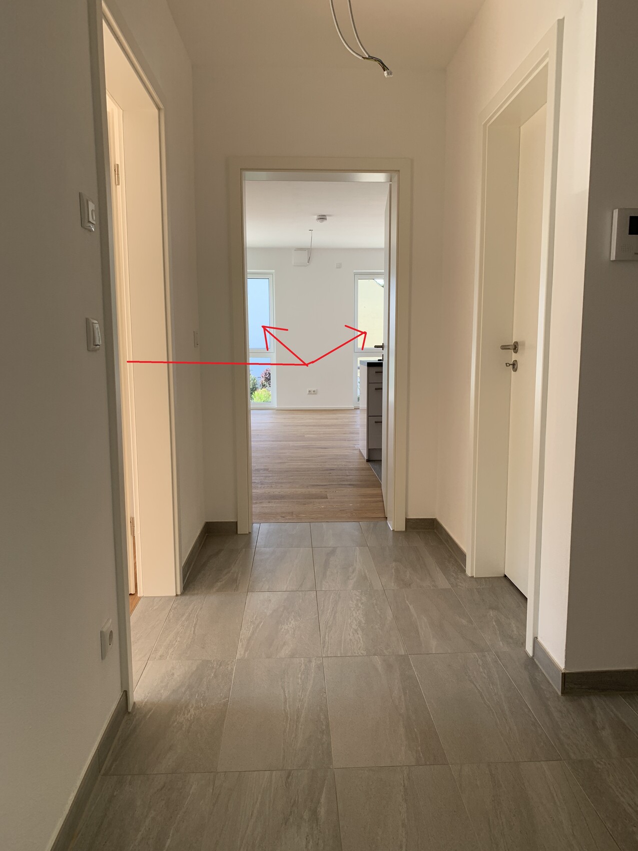 Hallenflur mit grauen Fliesen, offener Durchgang in Wohnbereich mit Holzboden.