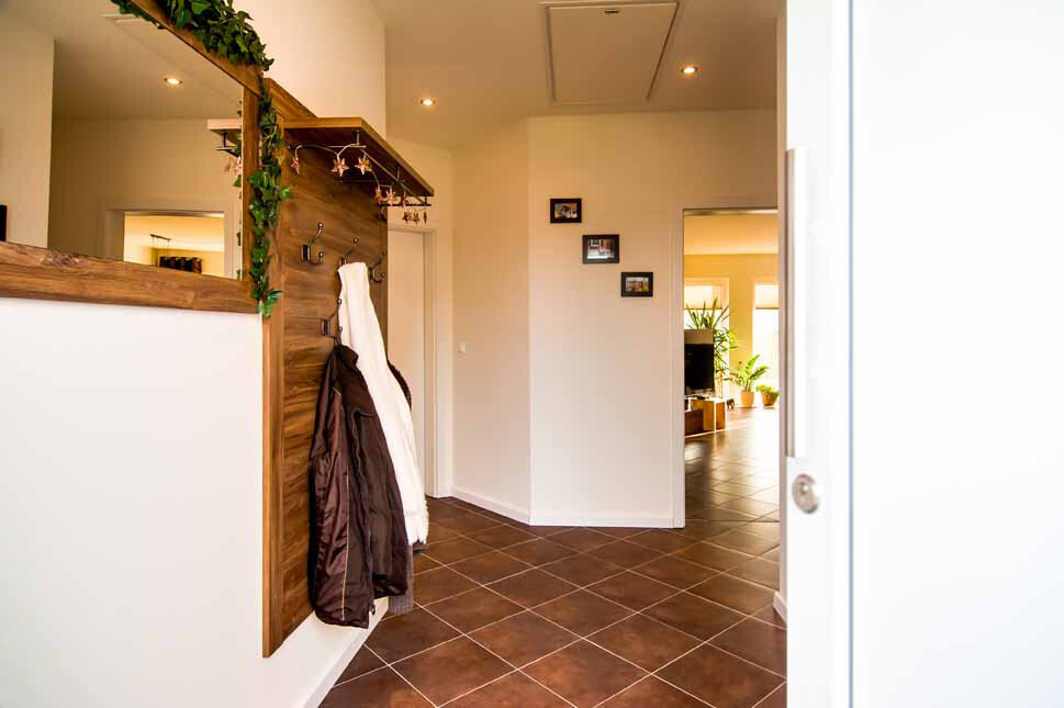 Heller Eingangsbereich mit Garderobe an Holzverkleidung, Fliesenboden, Blick ins Wohnzimmer