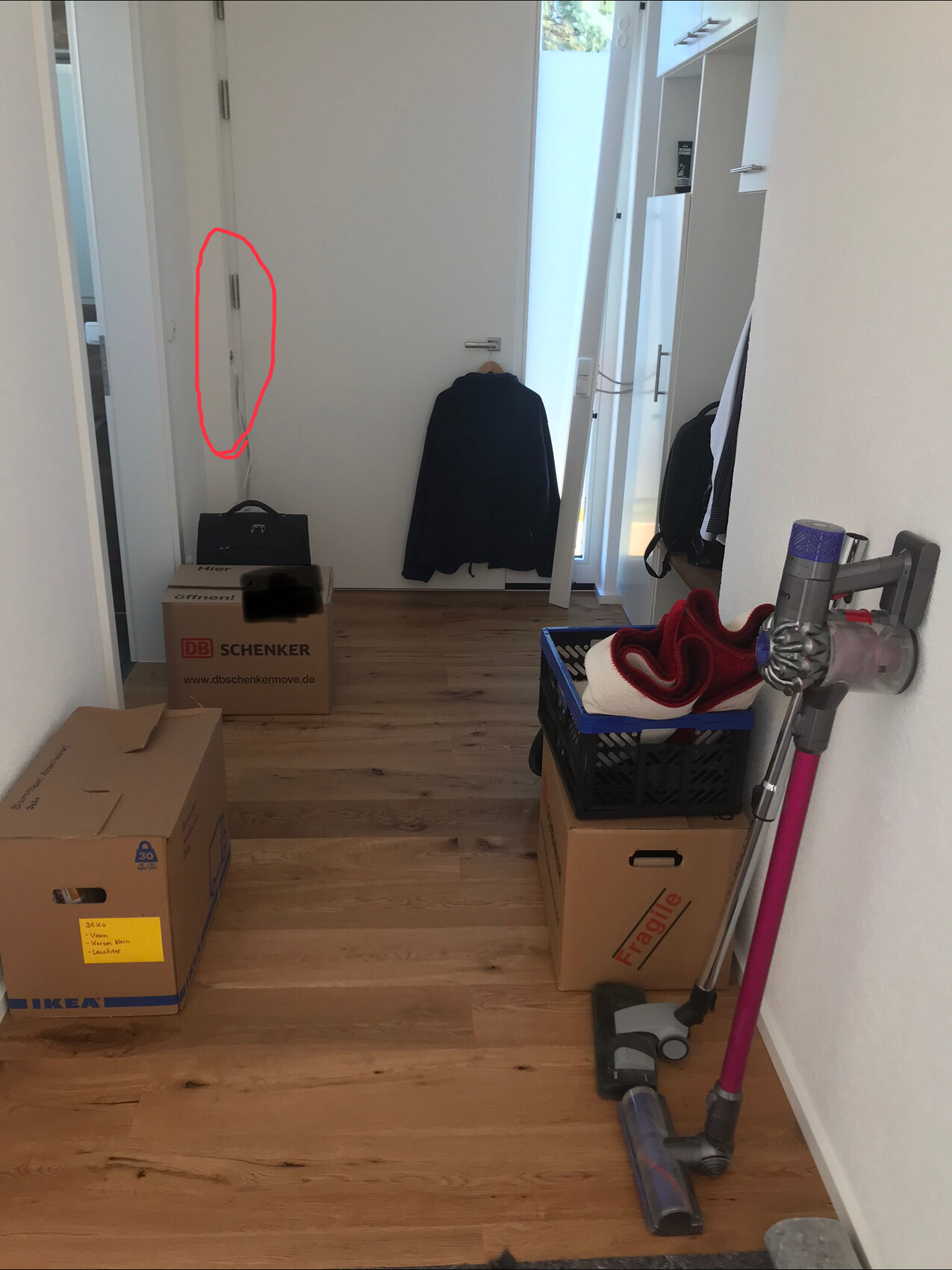 Heller Eingangsbereich mit Kartons, Staubsauger und Mantel am Türgriff.