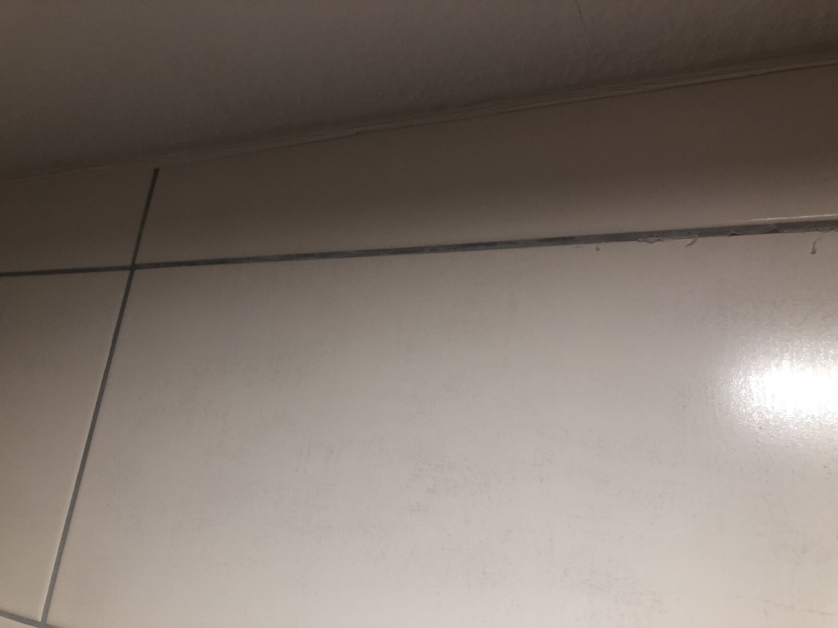 Nahaufnahme heller Bodenfliesen mit dunkler Fuge, Ecke nahe Wand Sockelleiste.