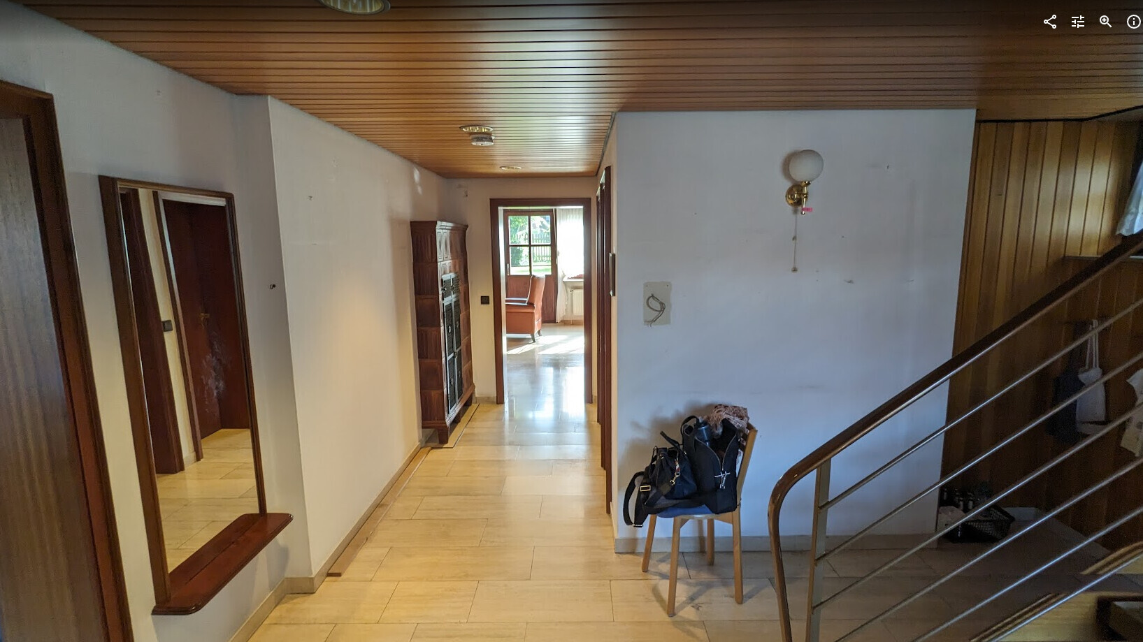 Heller Flur mit Holzdecke, Treppe rechts, Taschen auf Stuhl; Blick ins Wohnzimmer.