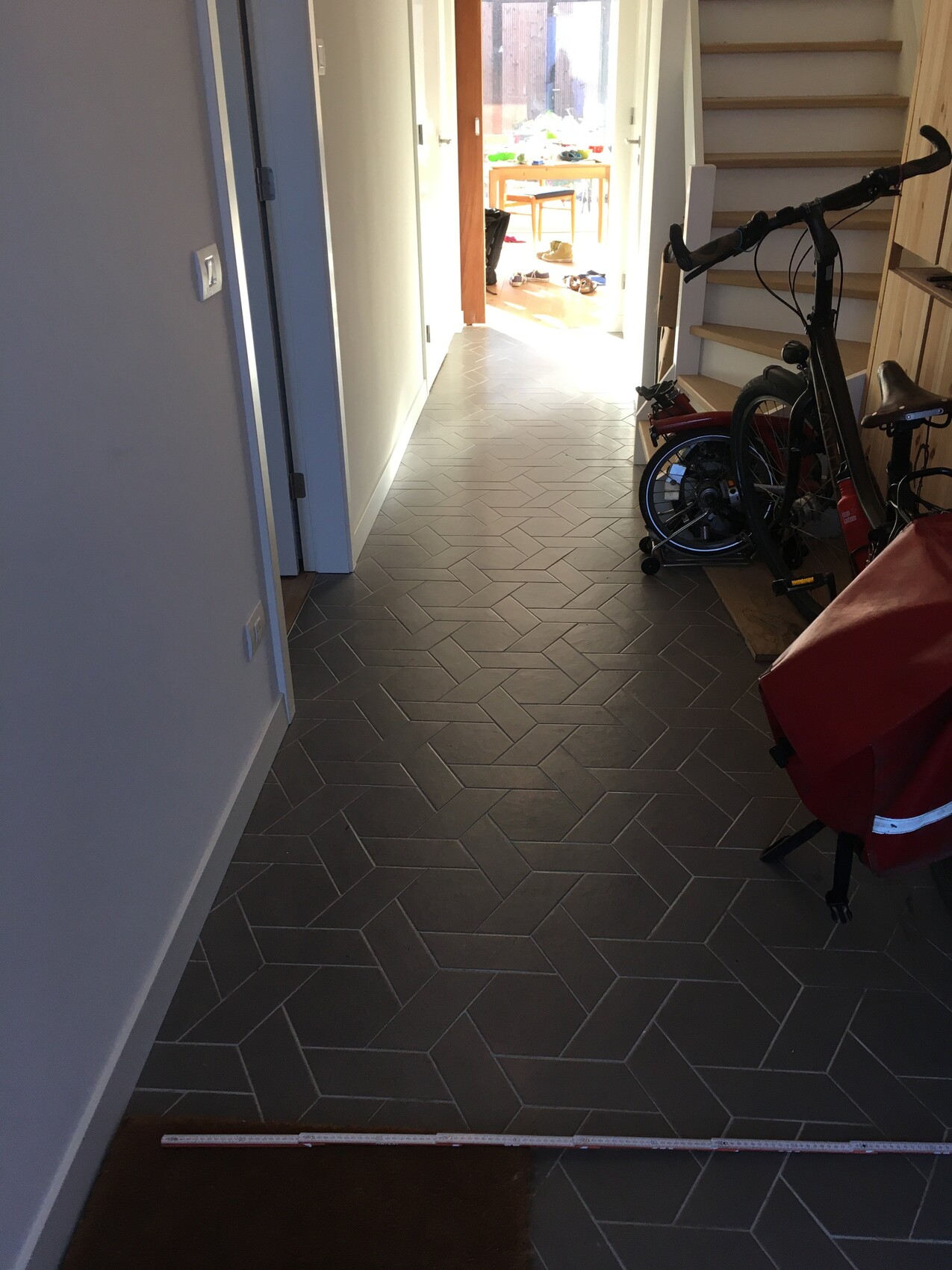 Heller Flur mit grauen Fliesen; rechts Fahrrad, Treppe, helles Zimmer am Ende.