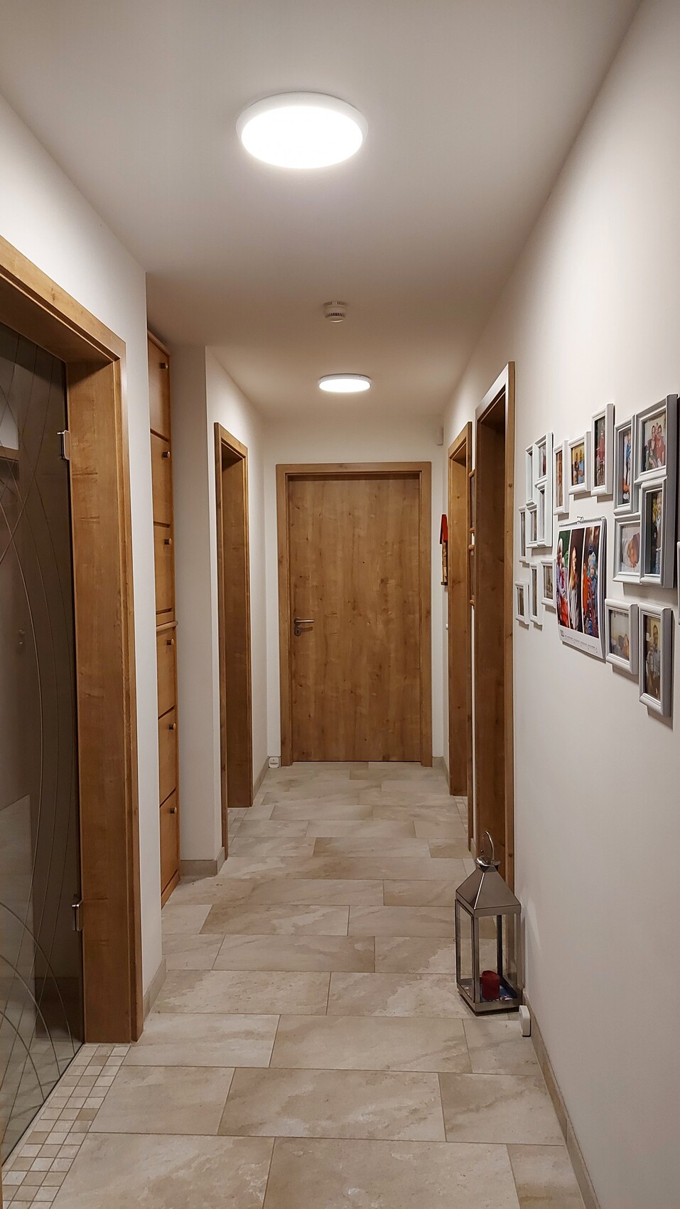 Heller Flur mit Holztüren, rechte Wand mit Bildergalerie aus Fotos, Laterne auf dem Boden.