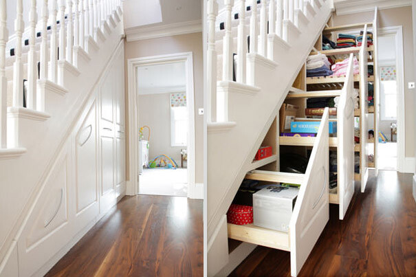 Heller Flur mit weißer Treppe; Stauraum darunter mit offenen Regalen, Kisten und Kleidung.