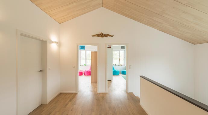 Heller Flur mit Holzfußboden und Holzdach; Türen zu zwei Räumen mit bunten Sitzsäcken.