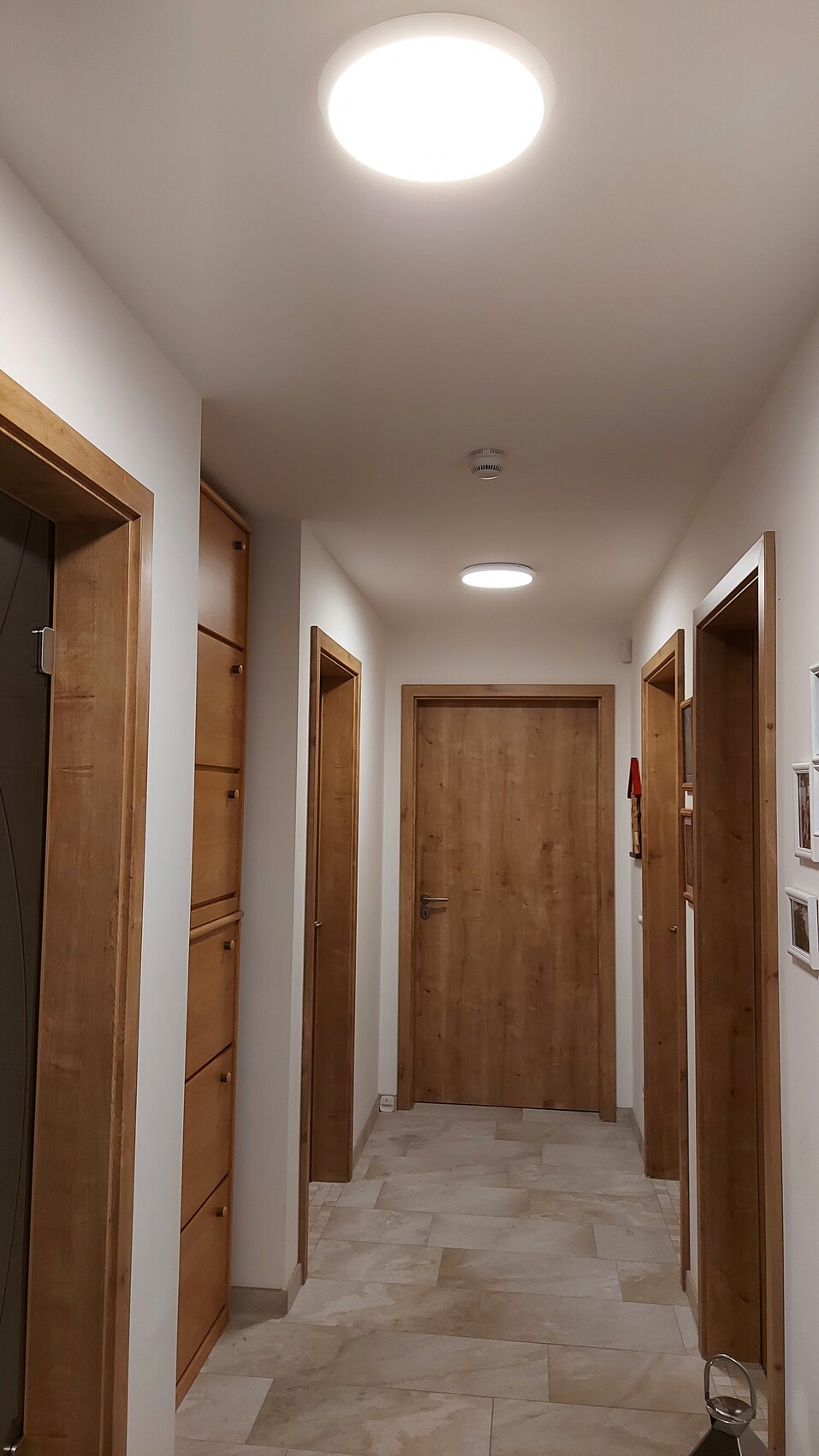Heller Flur mit Holztüren links und rechts, Fliesenboden, runde Deckenleuchte.