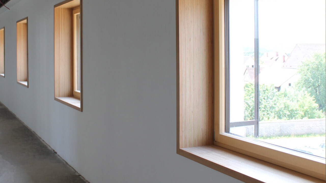 Heller Innenkorridor mit mehreren Holzfensterrahmen; Blick nach außen am Ende.