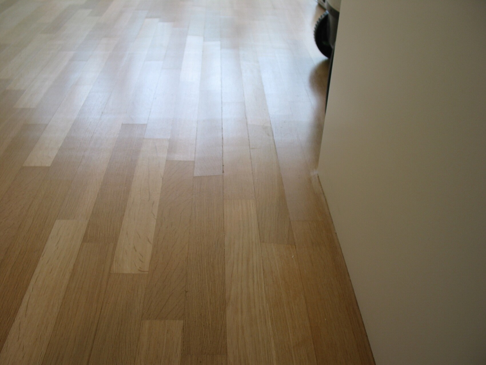 Heller Holzboden aus Holzdielen im Innenraum neben weißer Wand