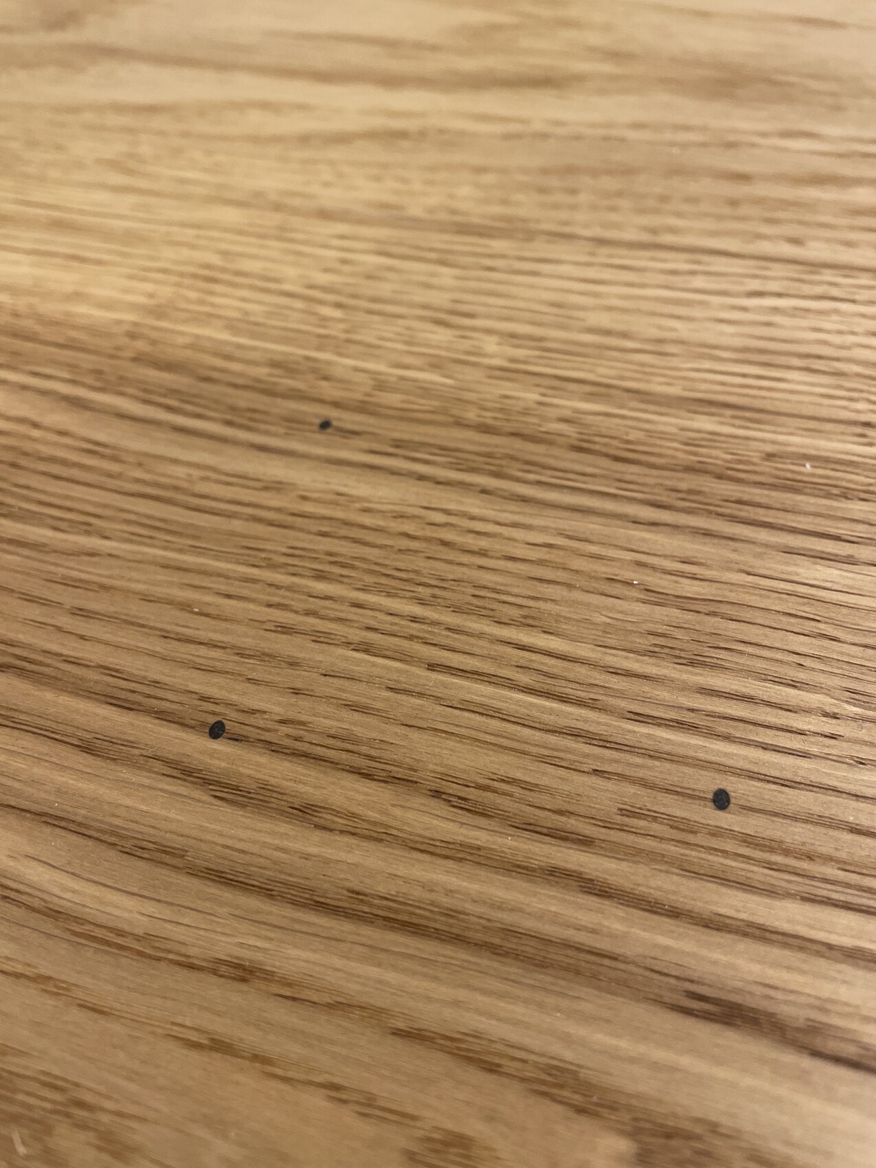 Holzoberfläche eines Tisches mit drei kleinen schwarzen Punkten.