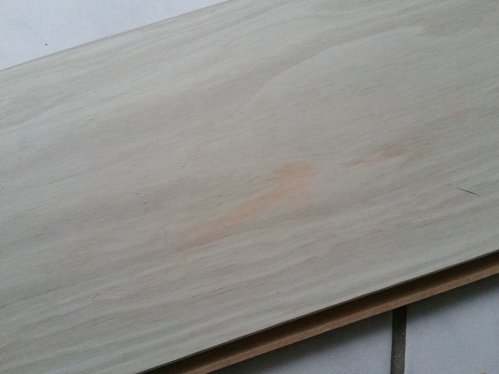 Heller Holzlatte mit orangefarbenem Fleck auf Fliesenboden