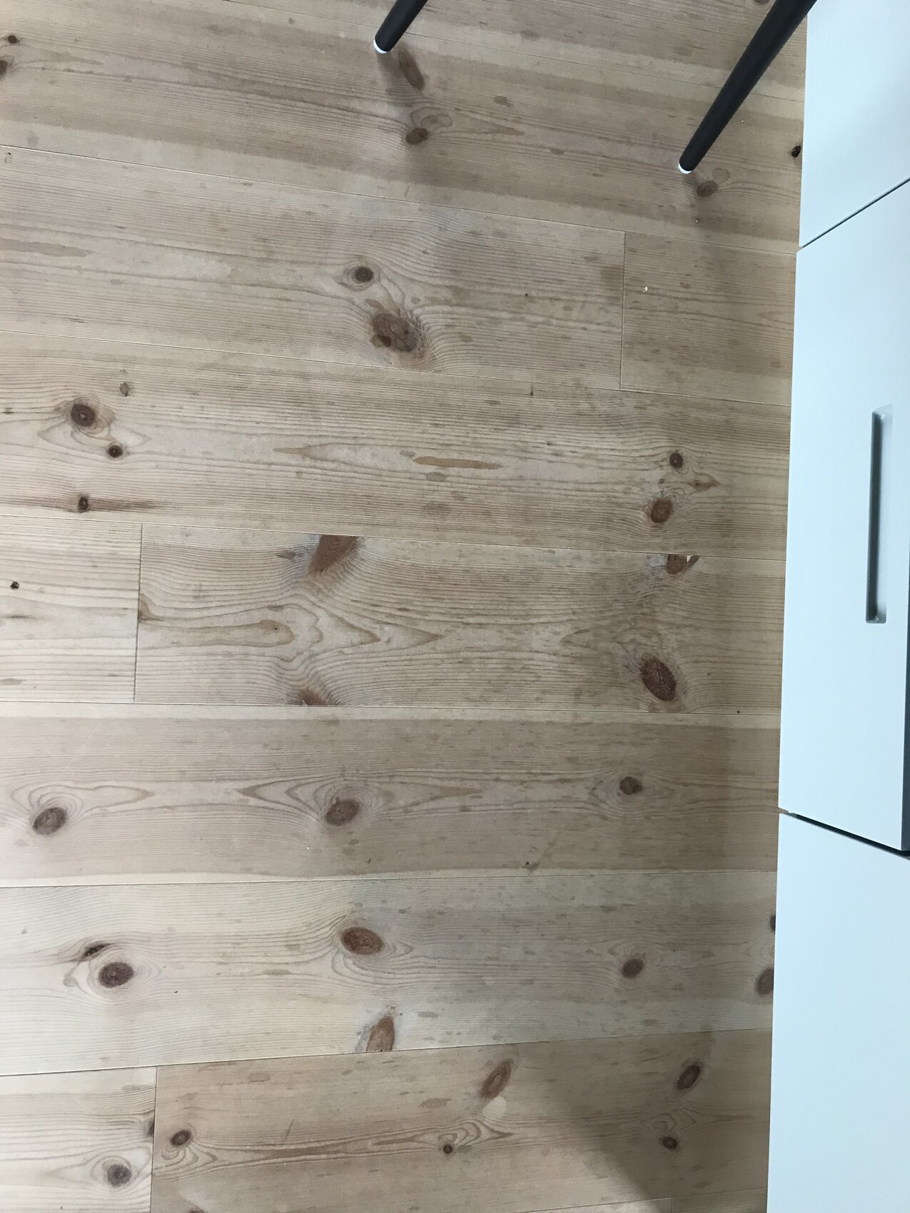 Heller Holzboden mit sichtbaren Knoten und weißem Küchenunterschrank am Rand