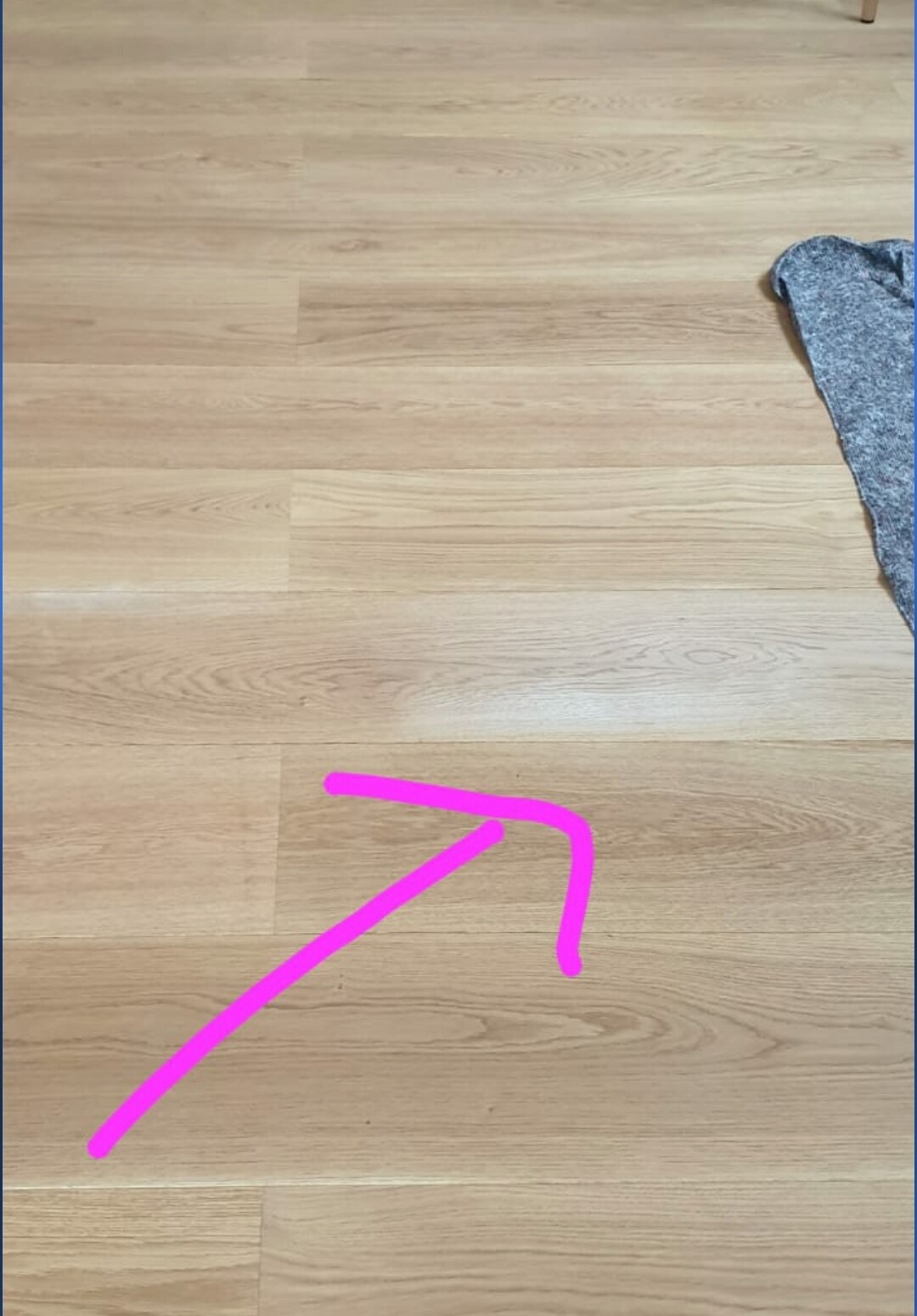 Heller Holzboden, pinker Pfeil verläuft nach rechts oben; graues Tuch am Rand sichtbar.