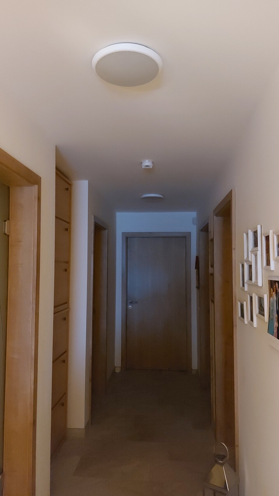 Heller Flur mit Holztüren rechts und links, Bilderrahmen an der Wand, Tür am Ende des Gangs.