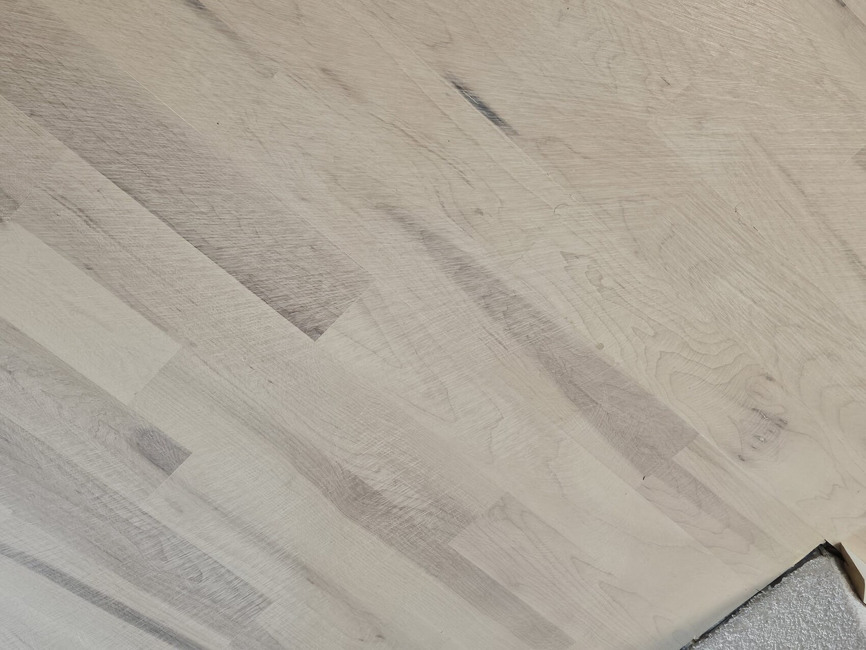 Heller Holzboden mit diagonalen, hellgrauen Brettern; Eckbereich sichtbar.