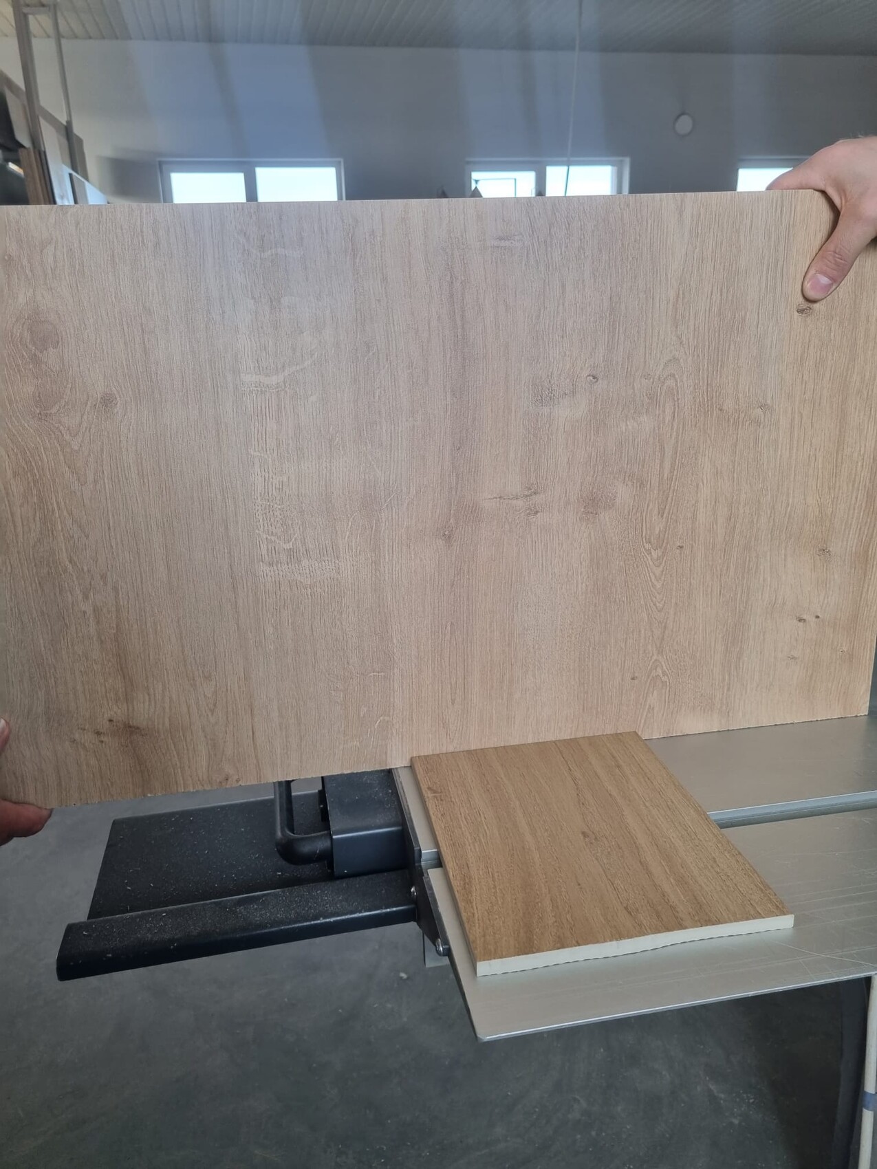 Große Holzplatte mit Maserung wird von Hand gehalten; daneben eine kleine Holzprobe auf Metall.