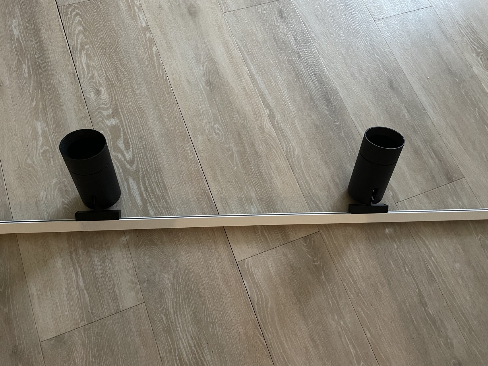 Zwei schwarze Spotlight-Module an einer weißen Stange auf hellem Holzboden.