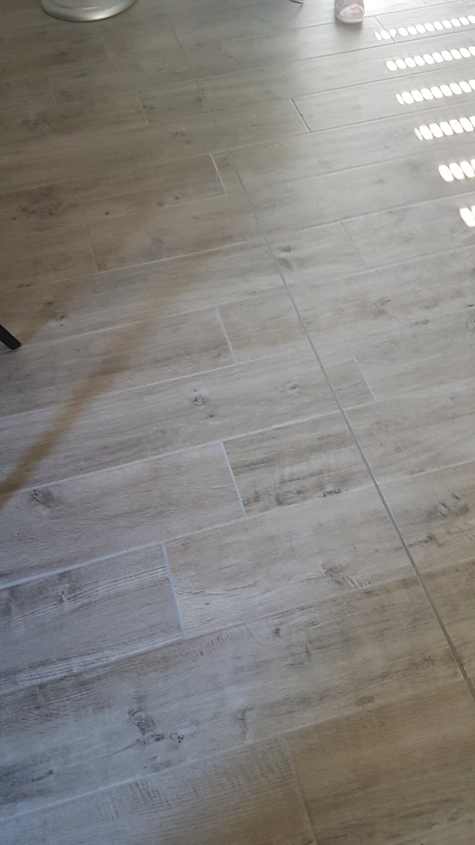 Heller Holzboden mit Maserung; Sonnenlichtpunkte rechts; Stuhlbein links unten sichtbar.