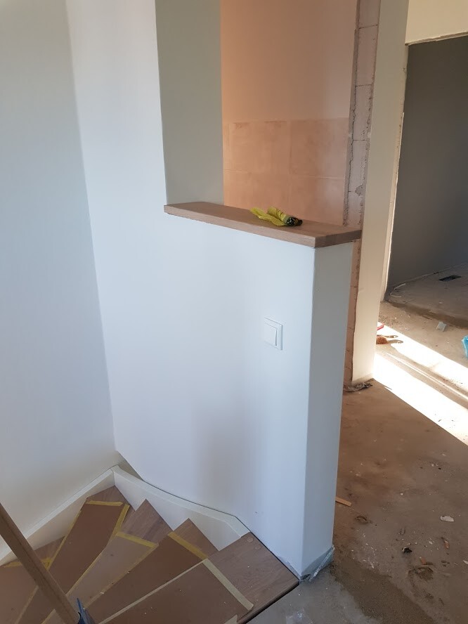 Untere Treppe im Bau: weiße Wände, Holzstufen, gelbe Handschuhe auf einem Holzbrett.