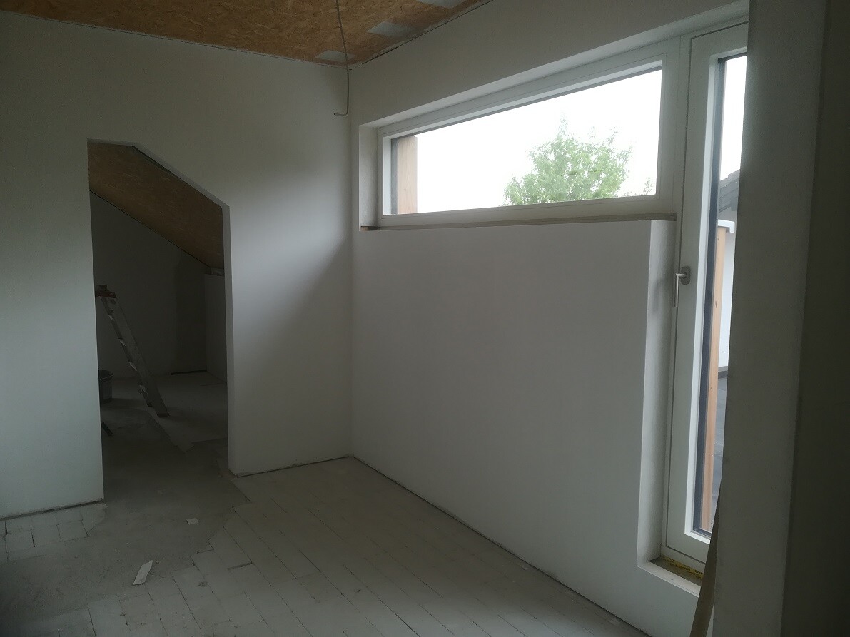 Unfertiger Innenraum im Loft: weiße Wände, Leiter, hohes Fensterband, Nischenbereich.