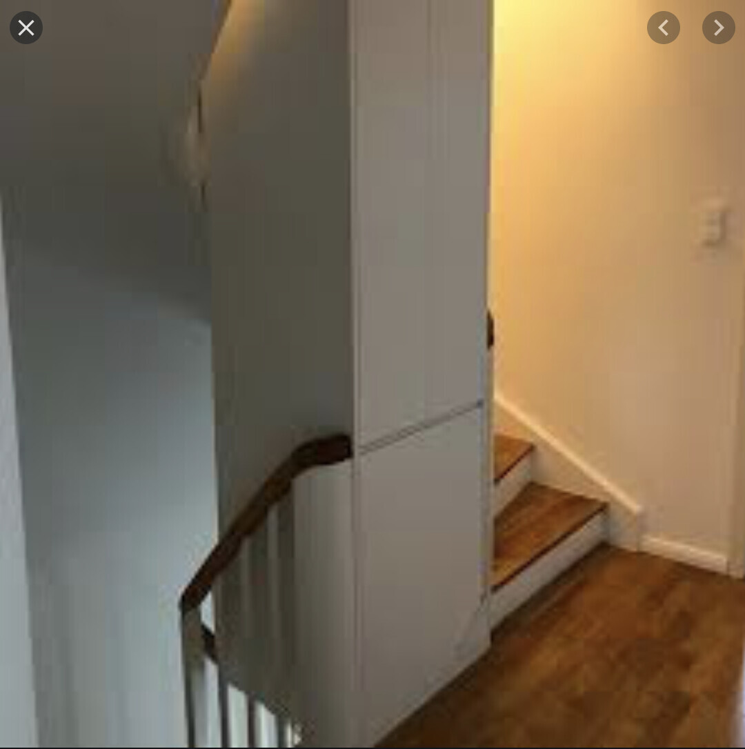 Innenansicht eines Treppenhauses: Holztreppe rechts, Holzboden, weißer Wandschrank links.
