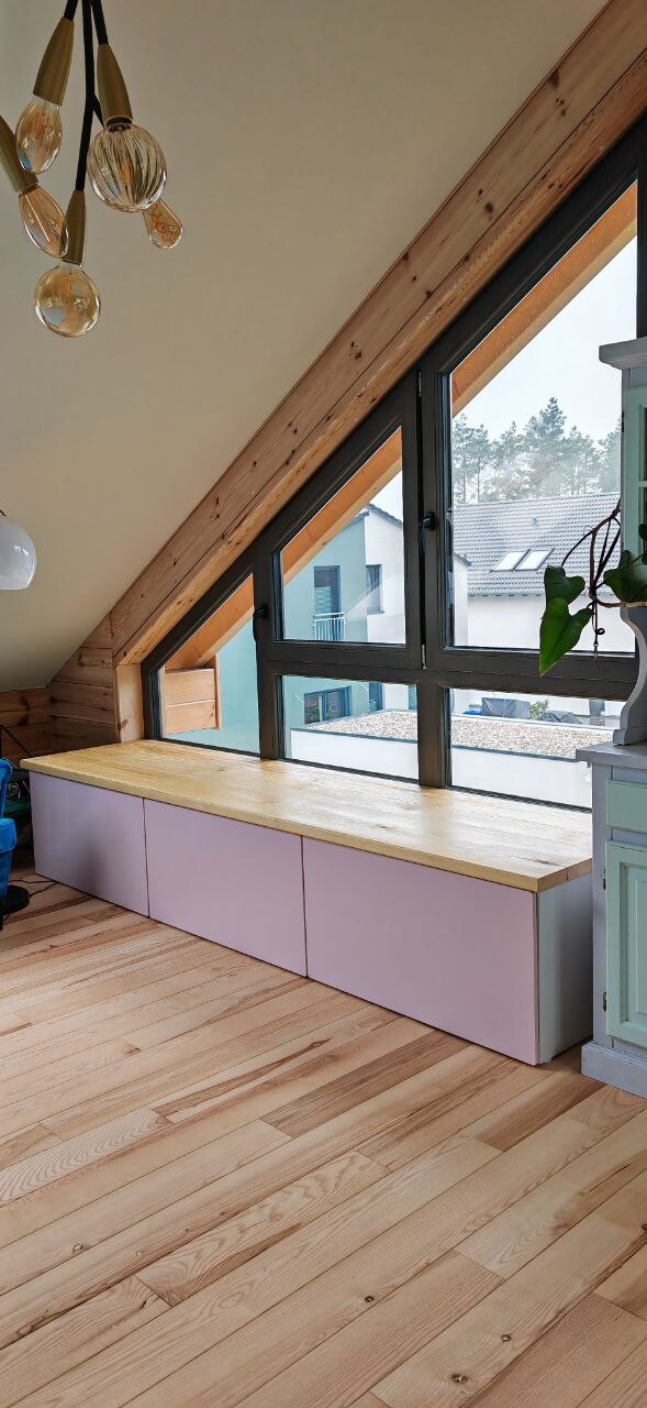 Helles Zimmer mit schrägen Fenstern, lange lavendelfarbene Schubladenboxen und Holzboden.