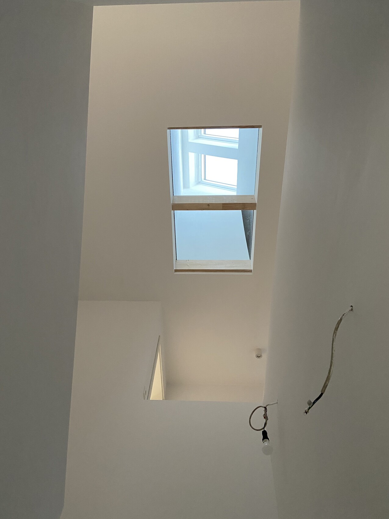 Heller Innenraum im Bau, Dachfenster in der Decke, sichtbare Elektroinstallation und Glühbirne.
