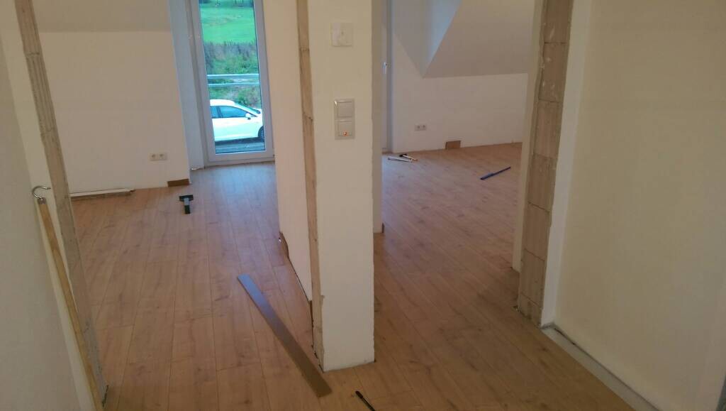Renovierter Innenraum mit Holzboden, Trennwand und verstreuten Bauwerkzeugen.
