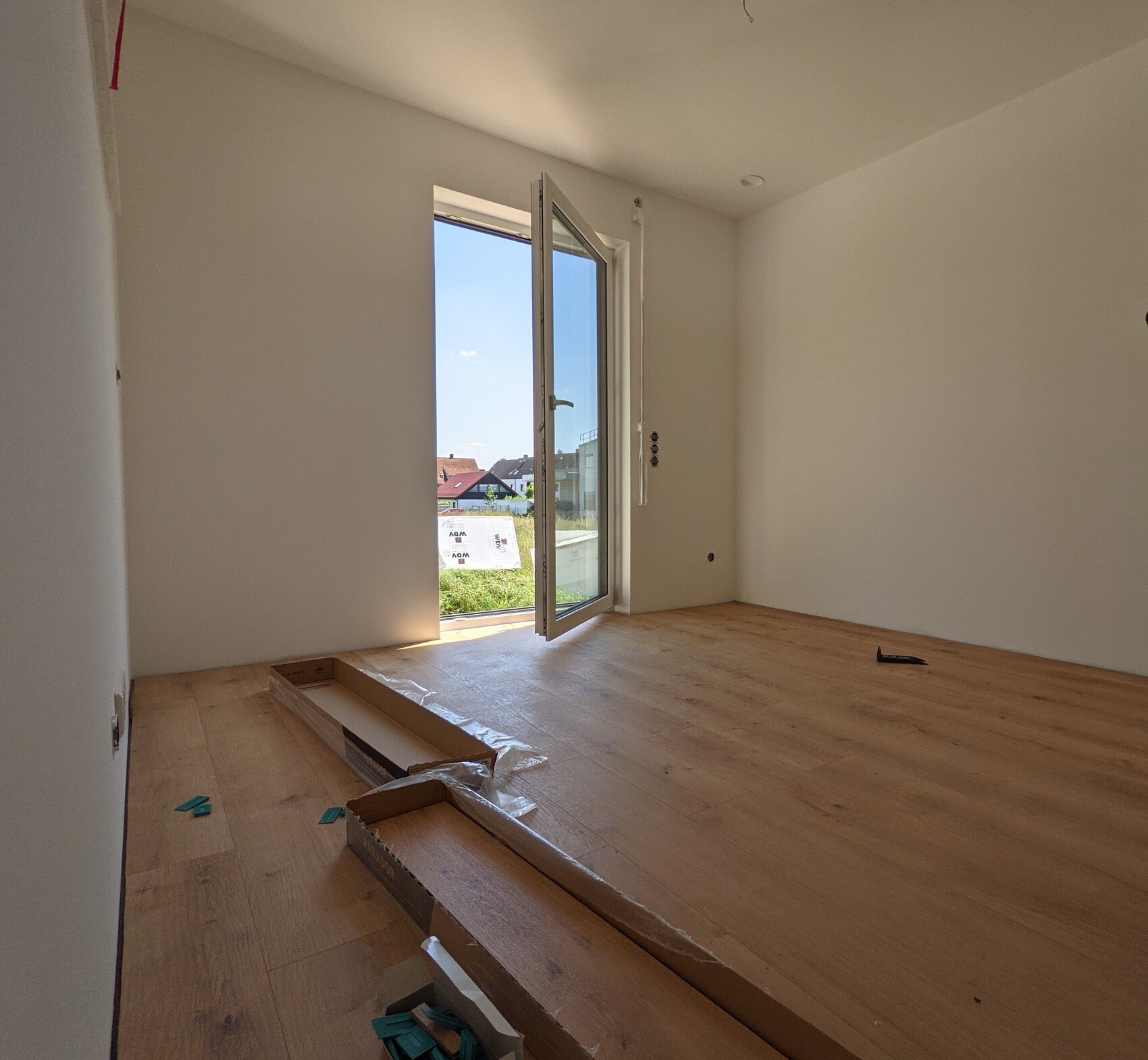 Leerer Wohnraum mit offener Glastür zum Balkon, Holzboden, Baumaterialien auf dem Boden.