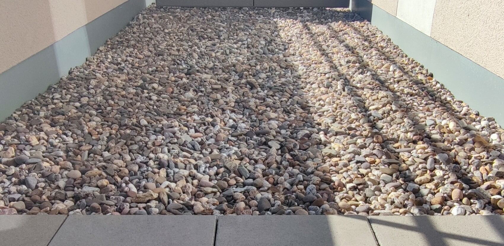 Schmaler Kiesweg zwischen Gebäudewänden, Boden mit kleinen Steinen bedeckt.