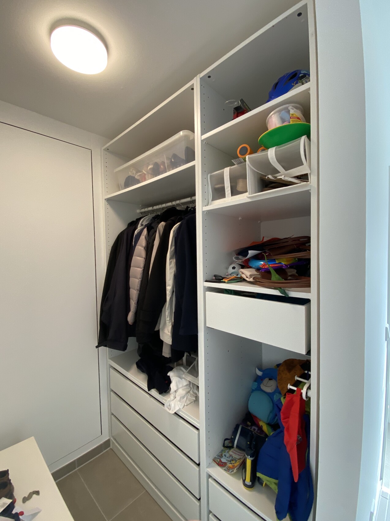 Offener Kleiderschrank mit Mänteln, Boxen, Taschen und Schubladen.