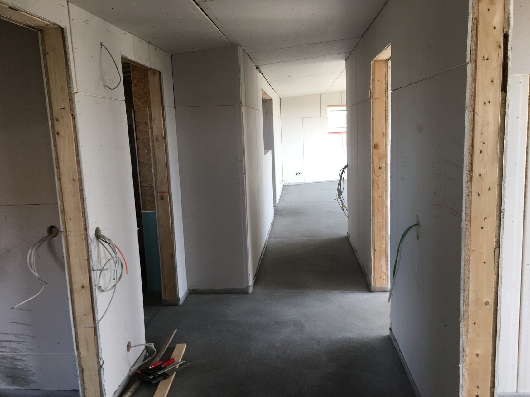 Heller Baukorridor im Rohbau mit freiliegenden Kabeln und offenen Türrahmen.