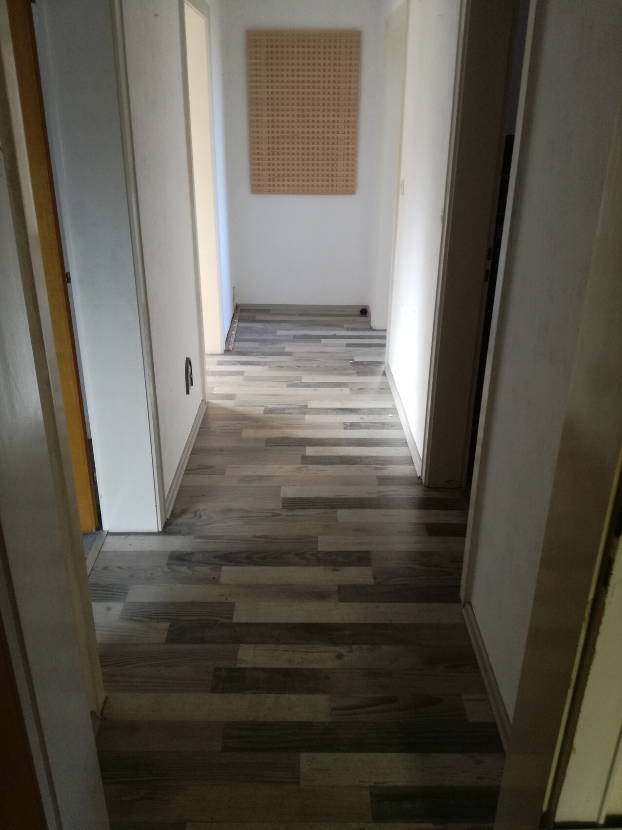 Heller Flur mit Laminatboden, weißen Wänden; Endwand mit Pinnwand.