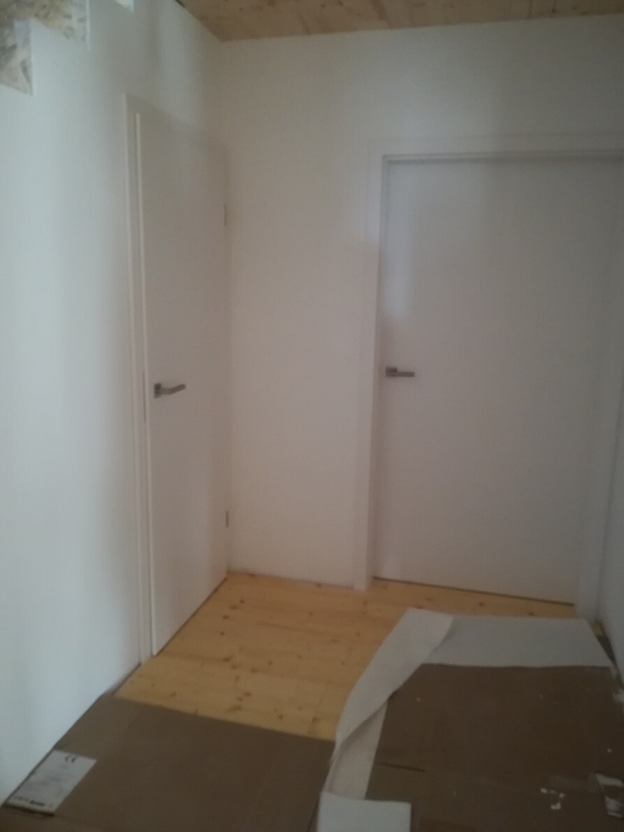 Flur mit weißen Innentüren, hellem Holzboden und Kartonresten auf dem Boden.