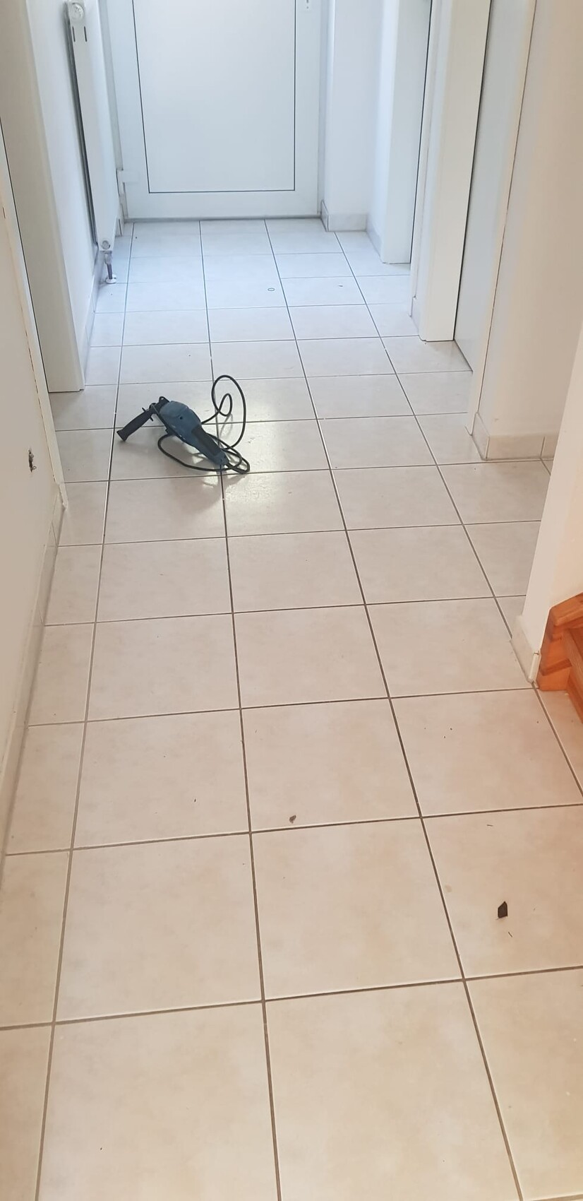 Heller Flur mit Tür am Ende; auf dem Boden liegt eine blaue Bohrmaschine mit Kabel.