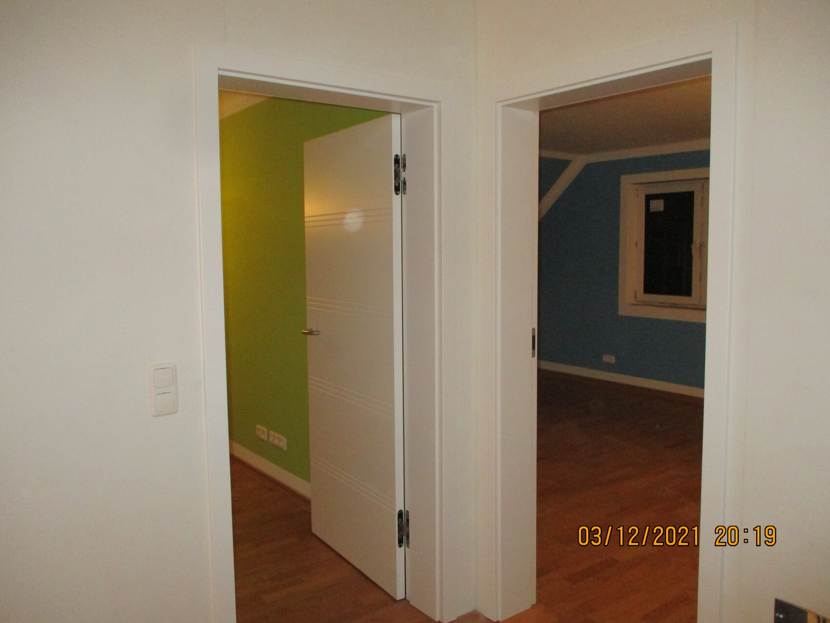 Zwei Türrahmen in Innenraum; links grüne Wand hinter offener Tür, rechts blaue Wand mit Fenster.