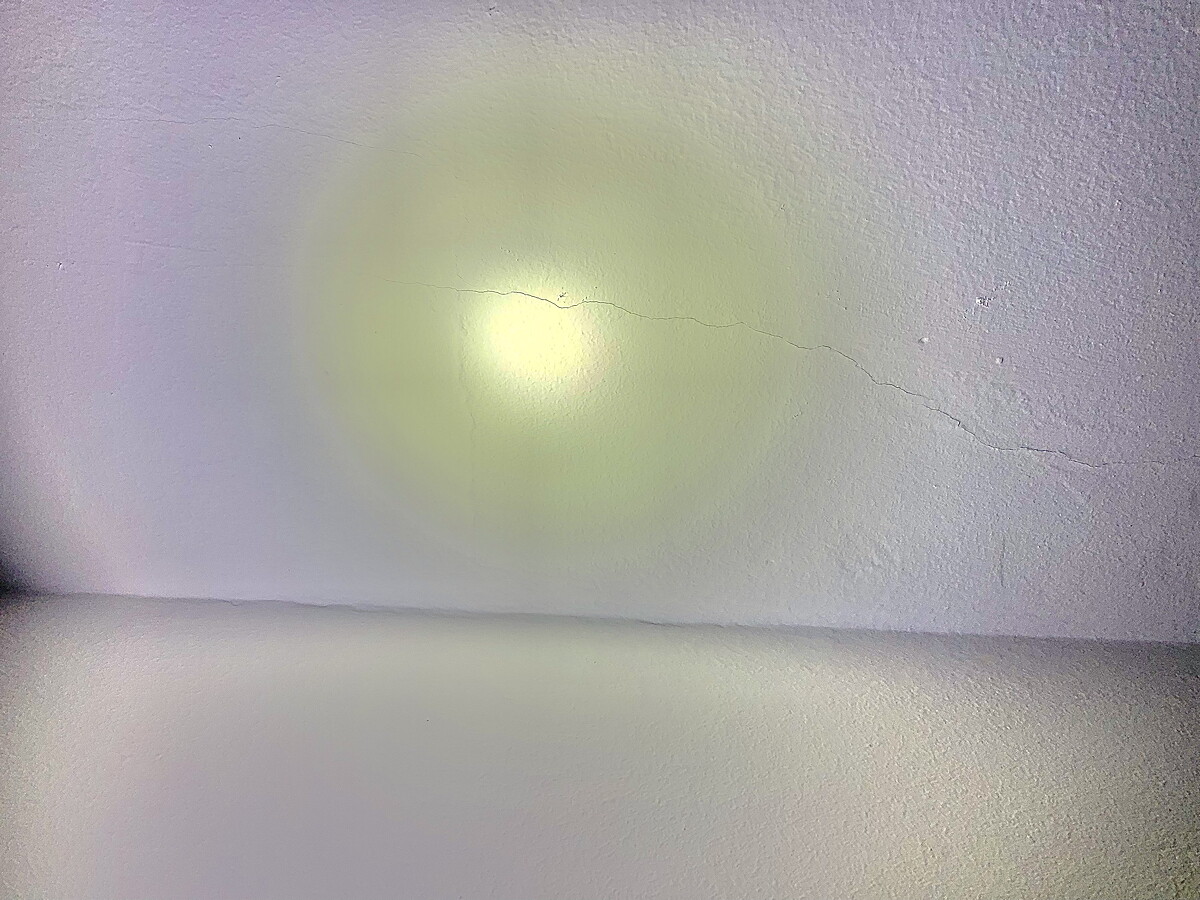 Weiße Wand mit gelblichem Lichthof, sichtbarer Haarriss und Boden unten.