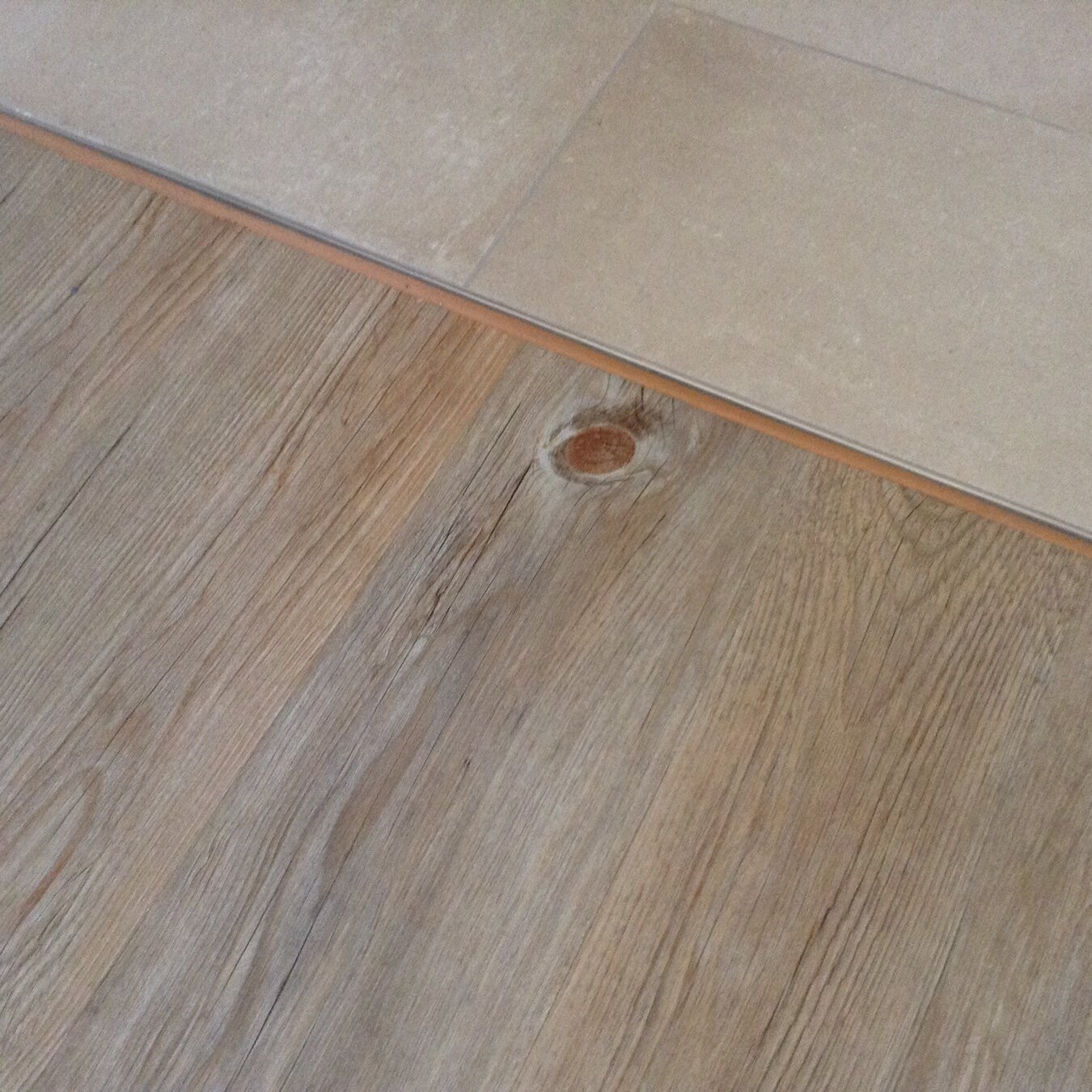 Nahaufnahme von Holzfußboden mit Knoten, Übergang zu hellen Fliesen.