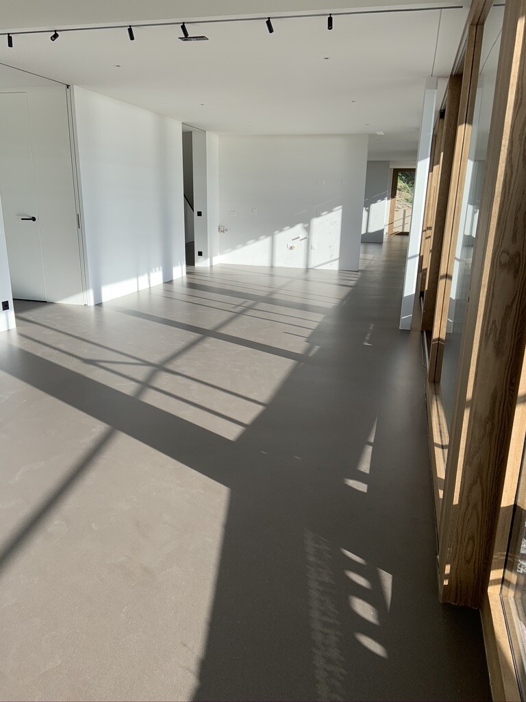 Heller leerer moderner Innenraum mit großen Fenstern, Holzrahmen und Schatten auf dem Boden.