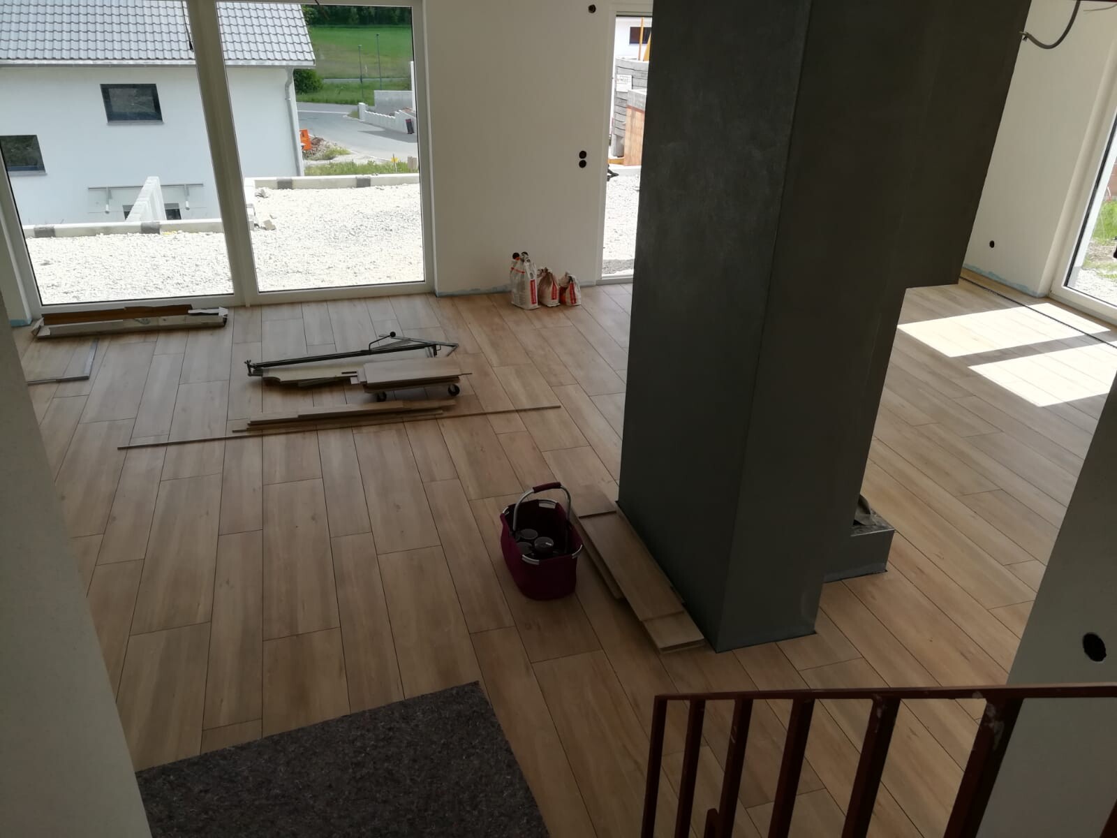 Innenraum im Bau: Laminatboden, Baumaterialien, grauer Stützpfeiler, große Fensterfront.