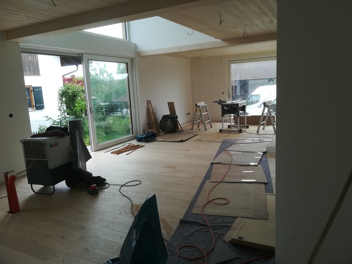 Renovierungsraum im Bau: Werkzeuge, Leiter, Holzboden, Glas-Schiebetür nach außen.