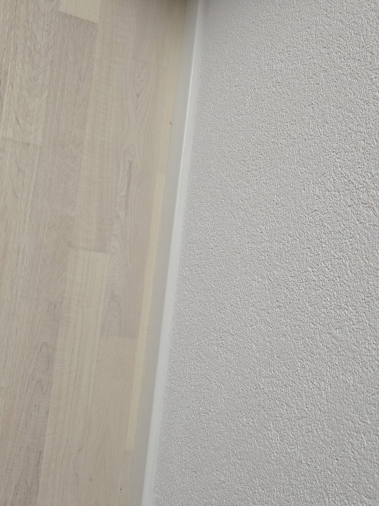 Boden aus hellem Holzlaminat links, weiße Wand rechts, schmale Fußleiste dazwischen.