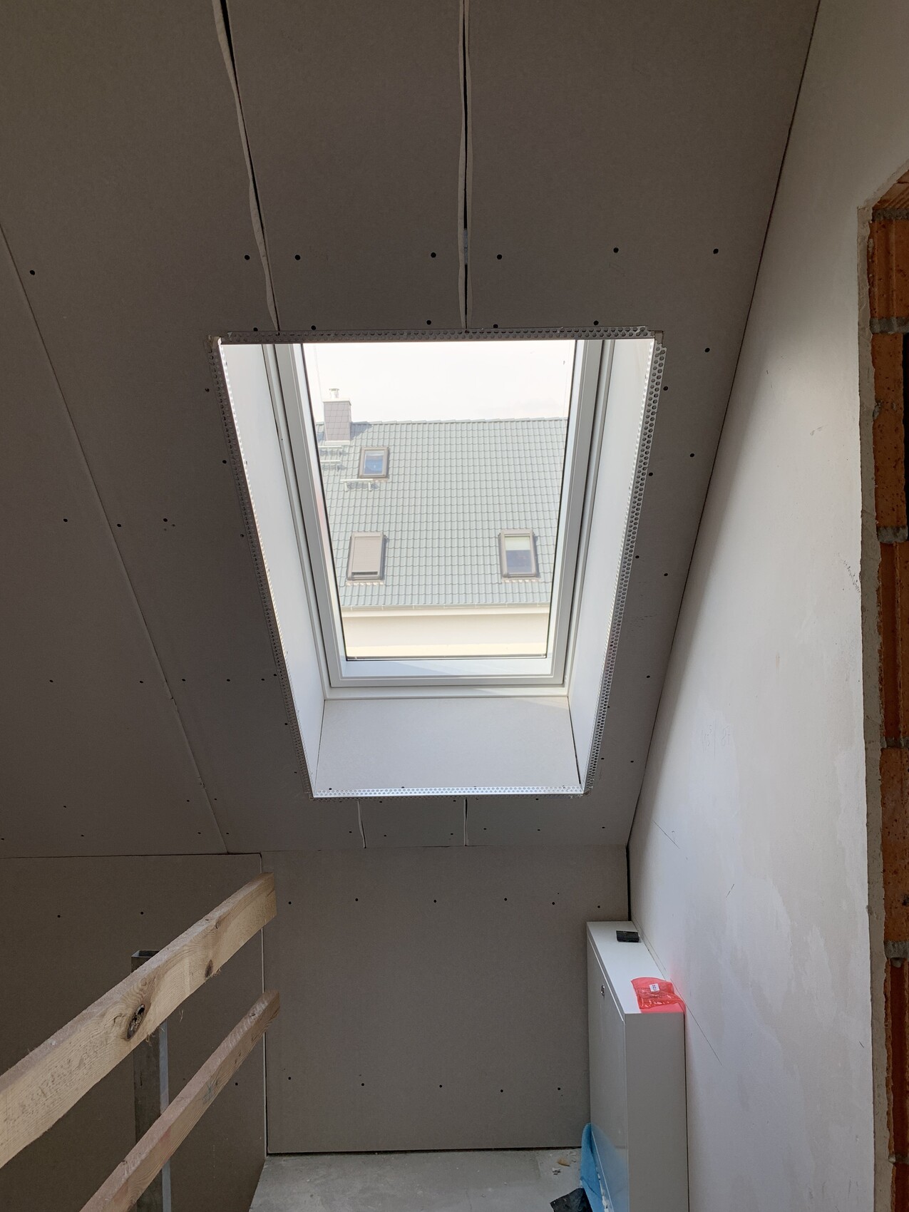 Bauraum mit Dachfenster, fertige Trockenbauwände, links Holzbalken, außen Dachziegel zu sehen