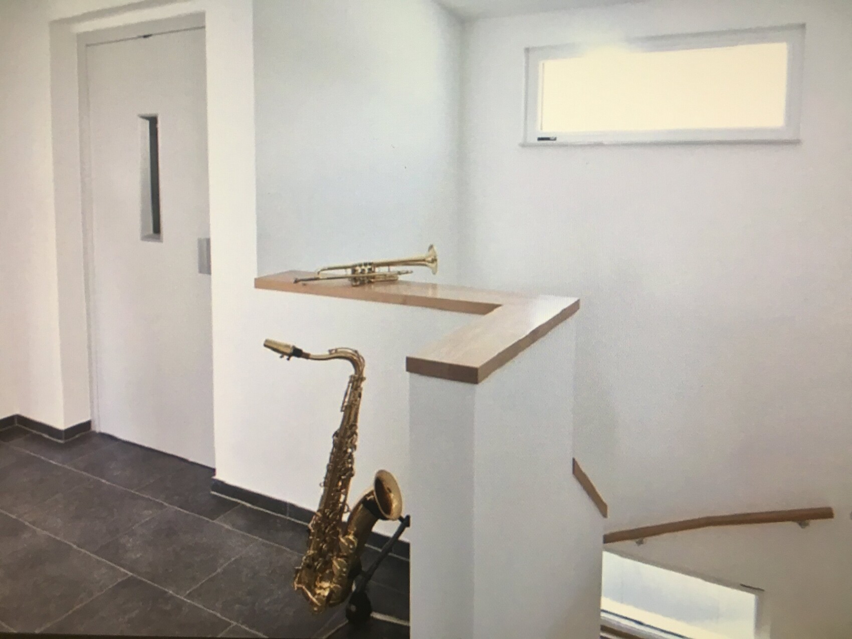 Treppenhaus: Trompete auf einer Holzablage, Saxophon lehnt am Pfeiler neben der Treppe.