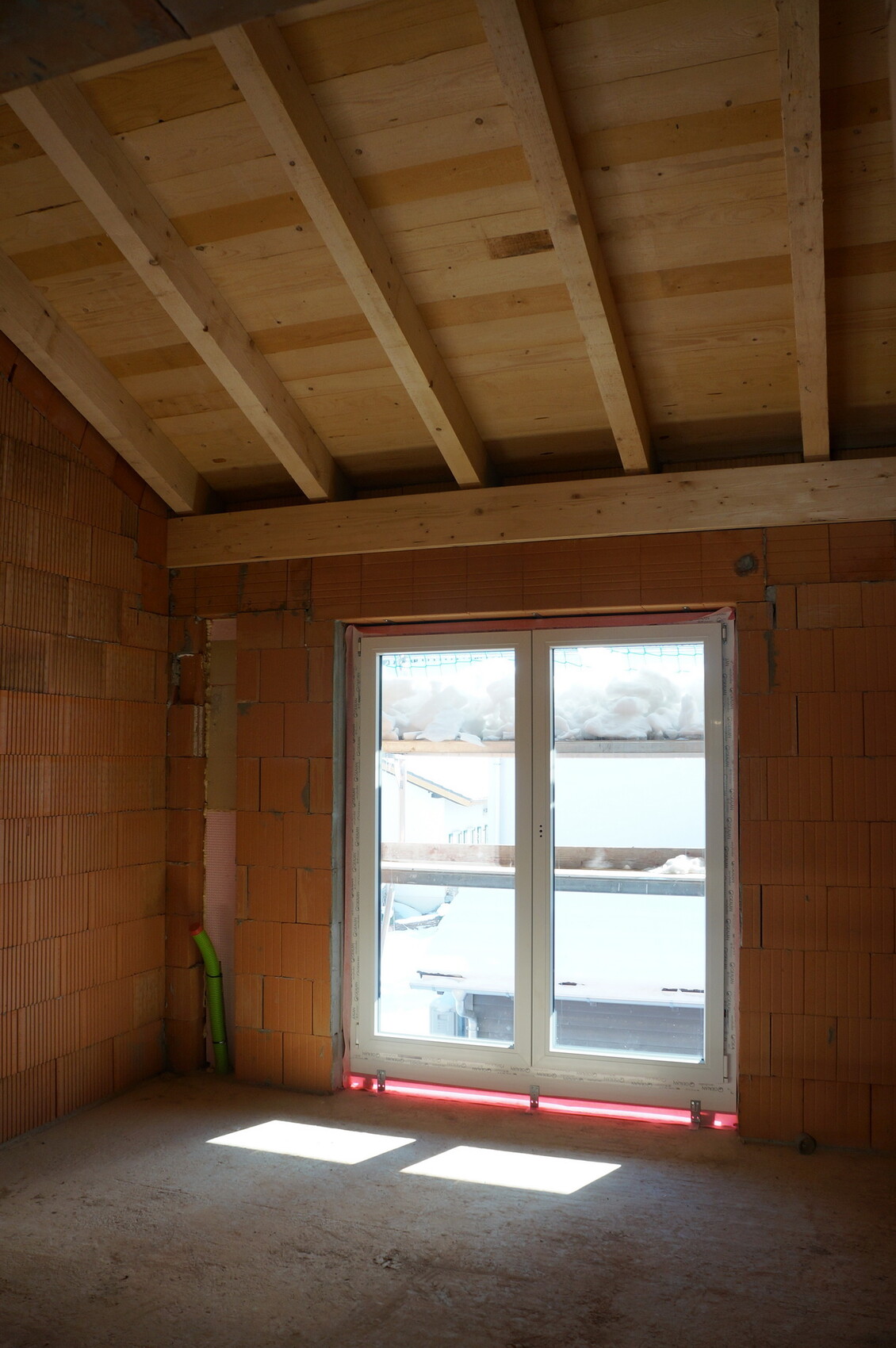 Rohbauzimmer mit Ziegelwänden, Holzbalkendecke und Fenster mit Schnee draußen.