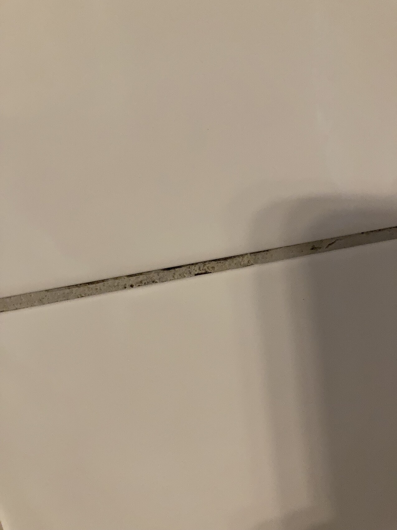 Schmutzige Fuge zwischen zwei hellen Flächen, Staub- und Ablagerungen sichtbar.