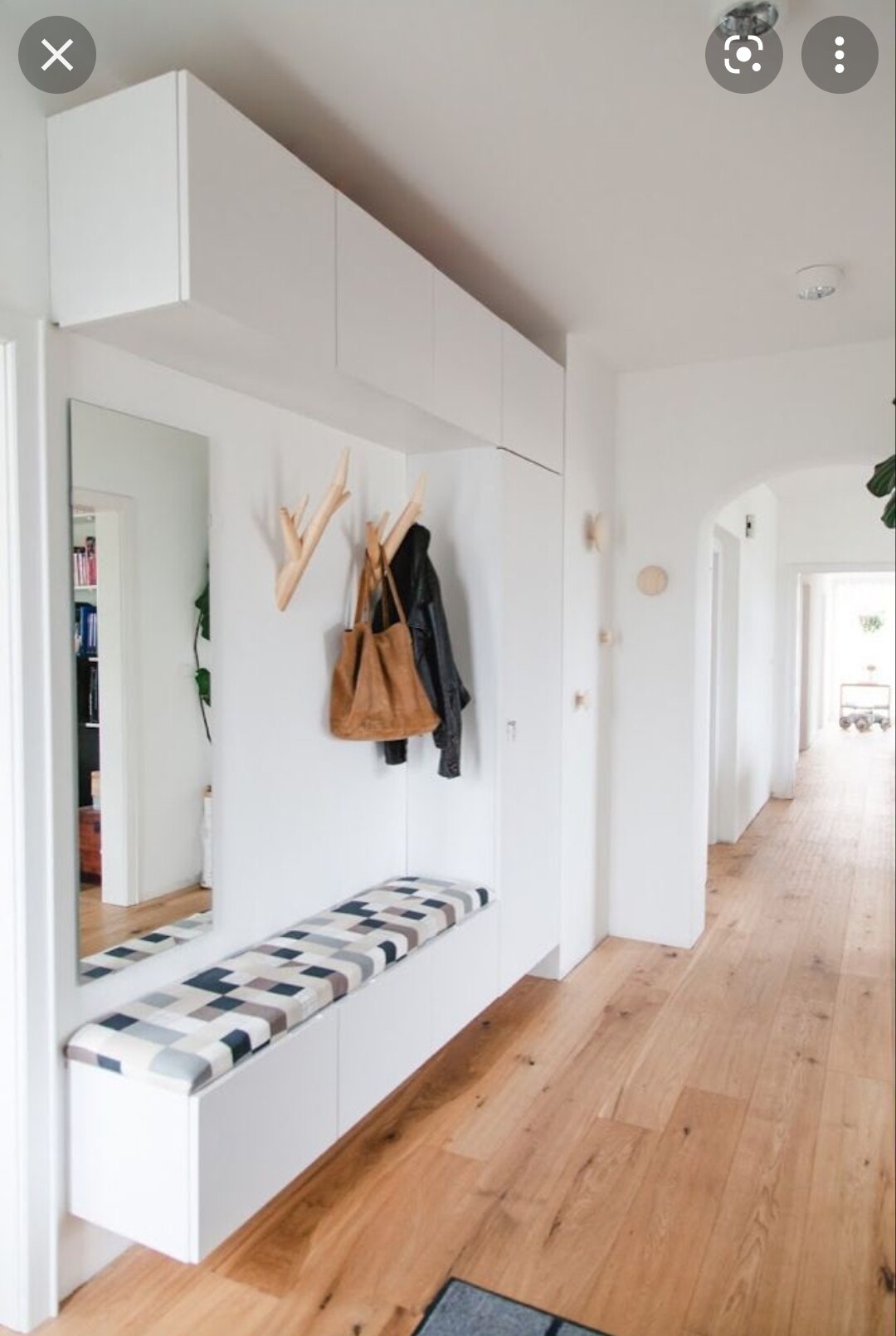 Heller Flur mit weißen Schränken, Garderobe, geometrisch gemusterte Sitzbank und Spiegel.