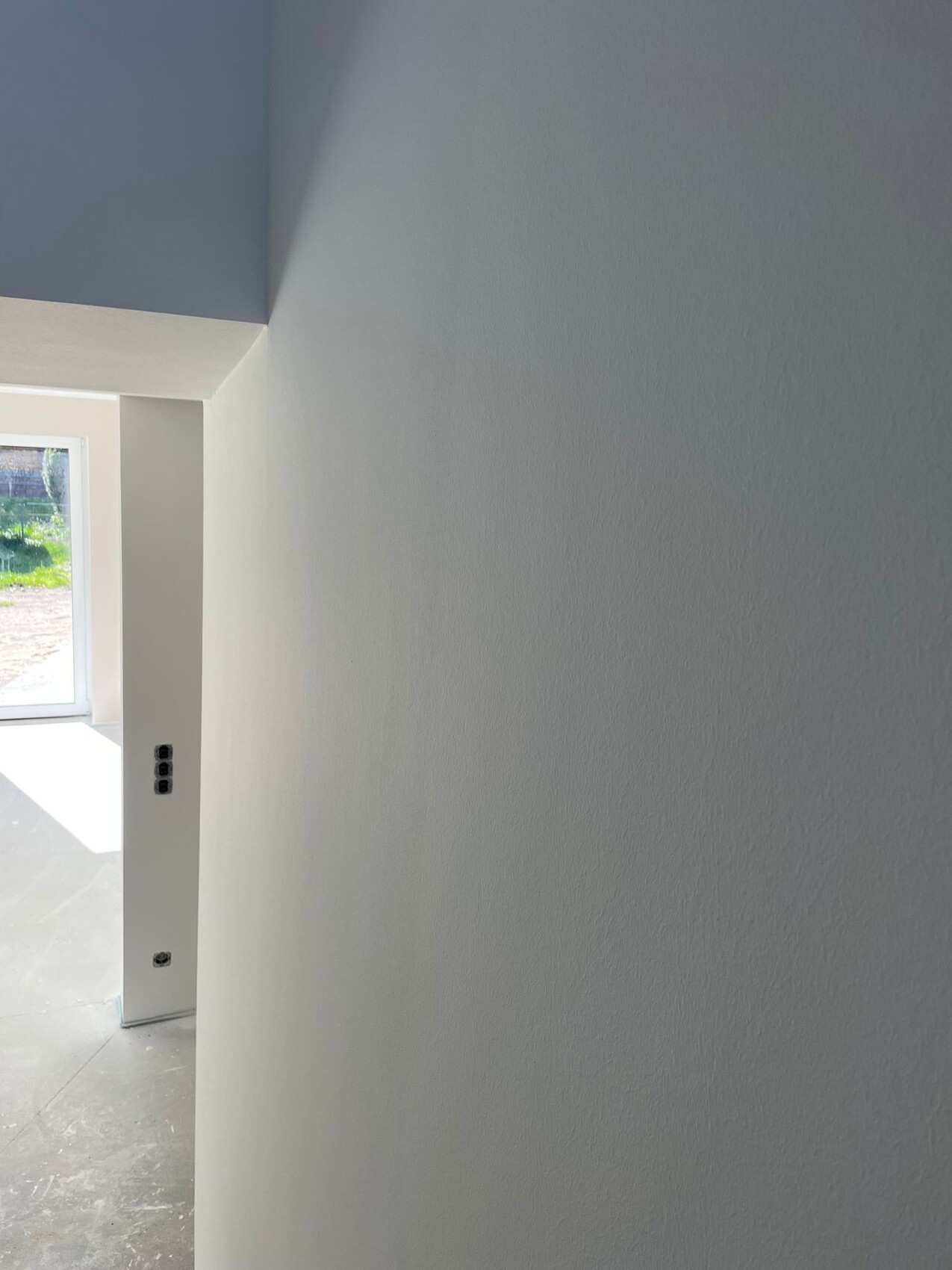 Heller Innenraum mit weißen Wänden, Fenster links und Steckdosen an der Wand.