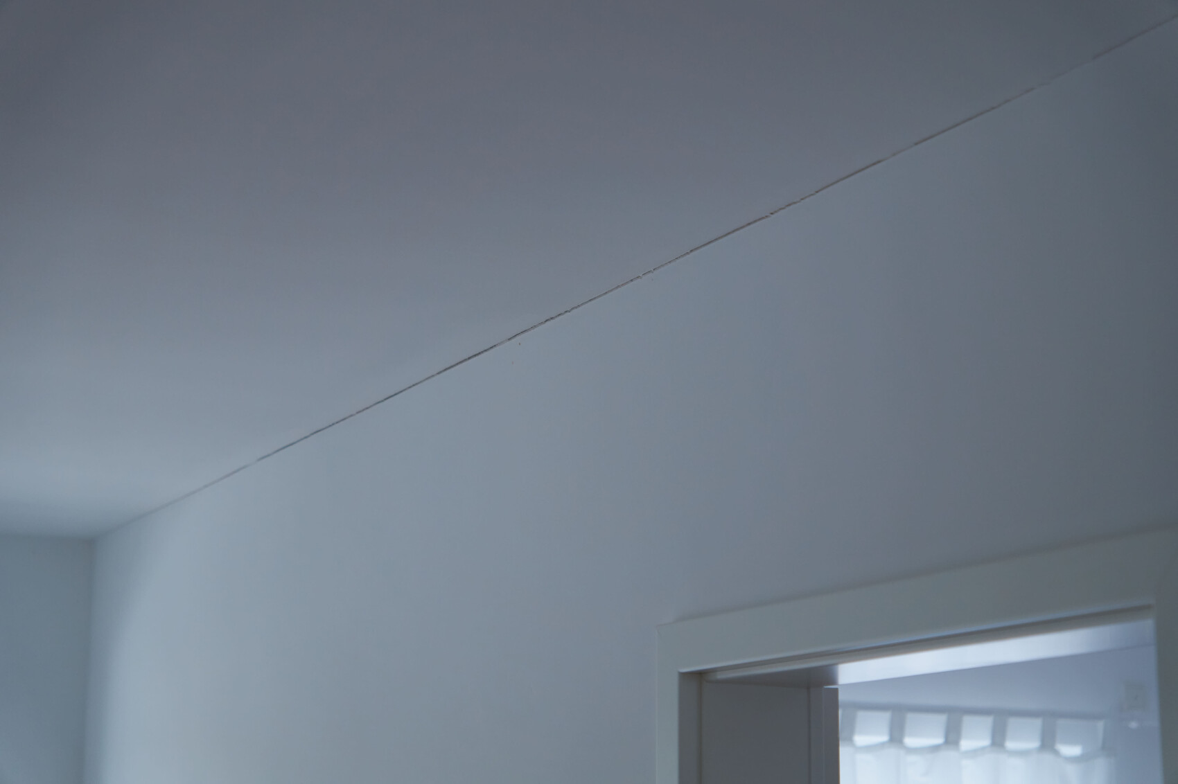 Blick in einen bläulich-grauen Innenraum: Decke, diagonale Linie, Türrahmen rechts.