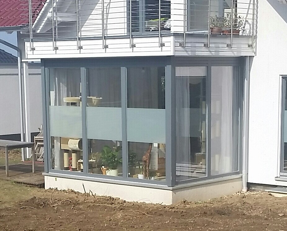 Moderne Glasveranda mit großen Fenstern Innenpflanzen und Balkon darüber vor dem Haus
