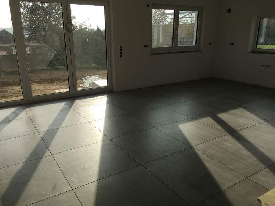 Heller, leerer Raum mit großen Fliesen, Glasfronten und Sonnenlicht.